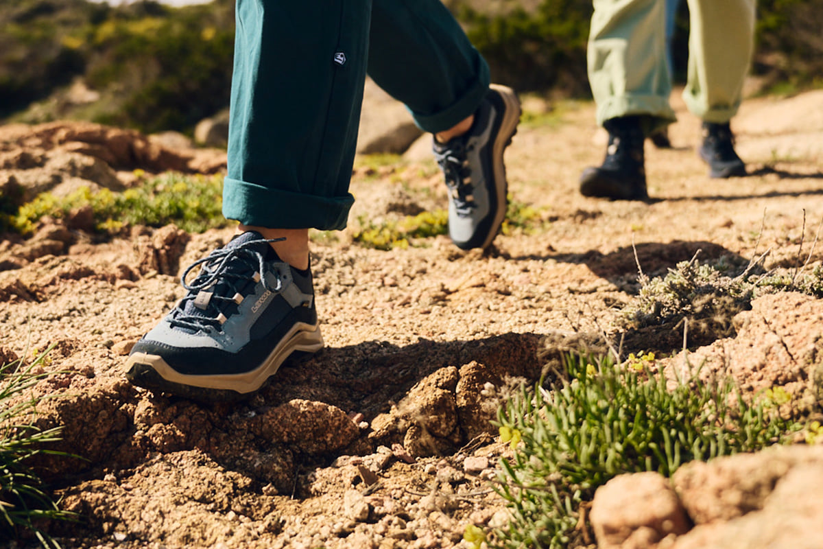 Active person wearing hiking boots on a rocky path surrounded by nature.