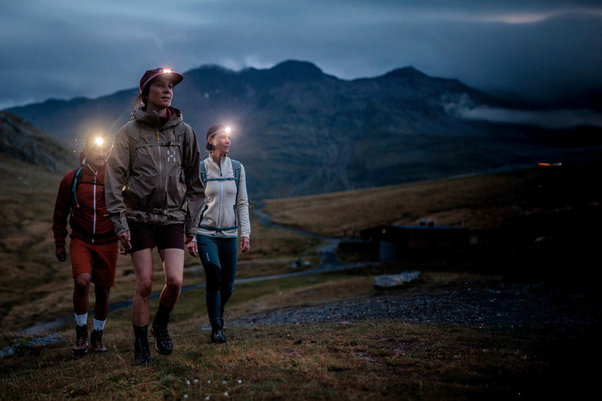 Three people wearing headlamps hiking in the mountains at night.