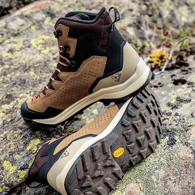 A pair of brown hiking boots rests on a moss-covered rock.